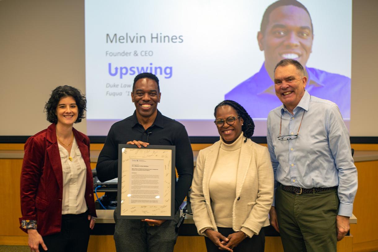Hines holds a print of the Upswing case study, signed by students, with (from left) Duke I&E Director Jamie Jones, Professor Ashleigh Shelby Rosette, and Professor Jon Fjeld